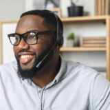 Young and handsome African-American employee wearing glasses, headphones with a microphone, talking to customers, communicating, and providing customer service on a helpline at the call center